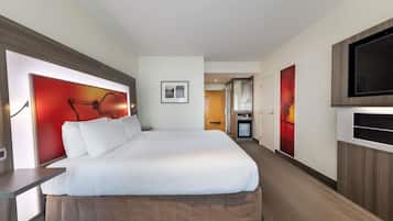 Habitación de hotel con una cama grande, televisor montado en la pared y un minibar.