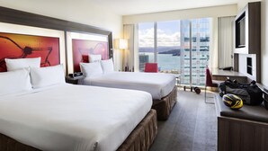 A hotel room with two beds, a desk, a chair, a TV, and a large window with a view of the sea. - Novotel Wellington (Wellington)