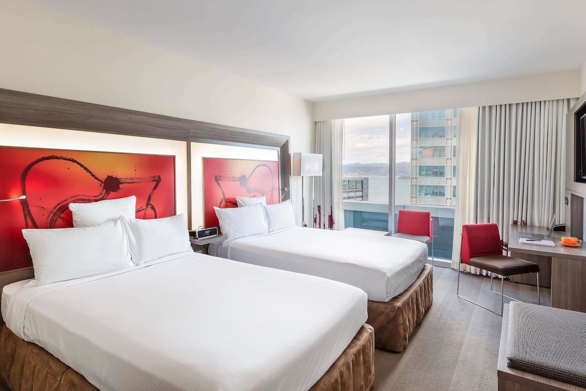 A hotel room with two beds, a desk, a chair, and a TV.