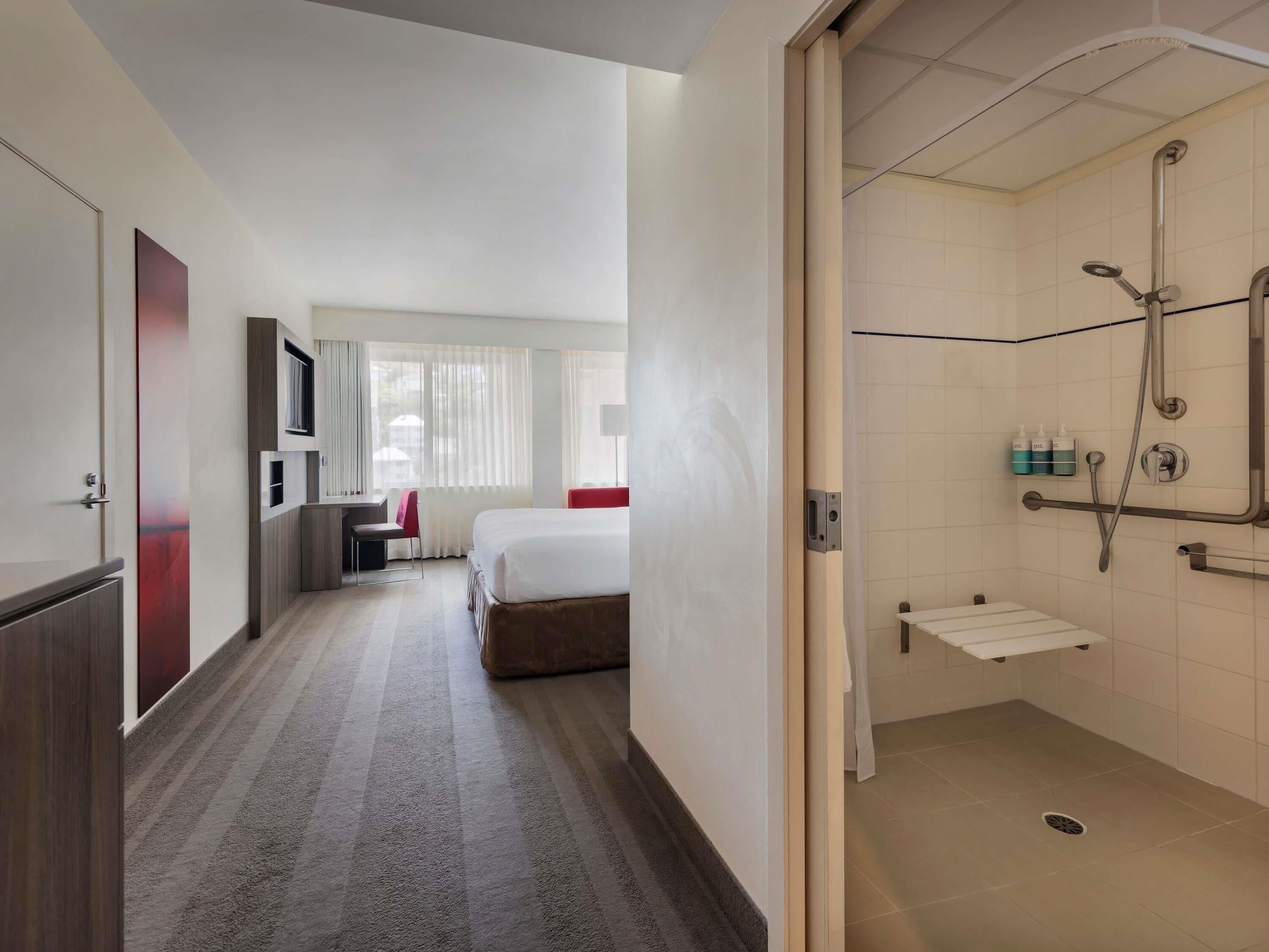 Habitación de hotel con ducha, cama, escritorio y silla.