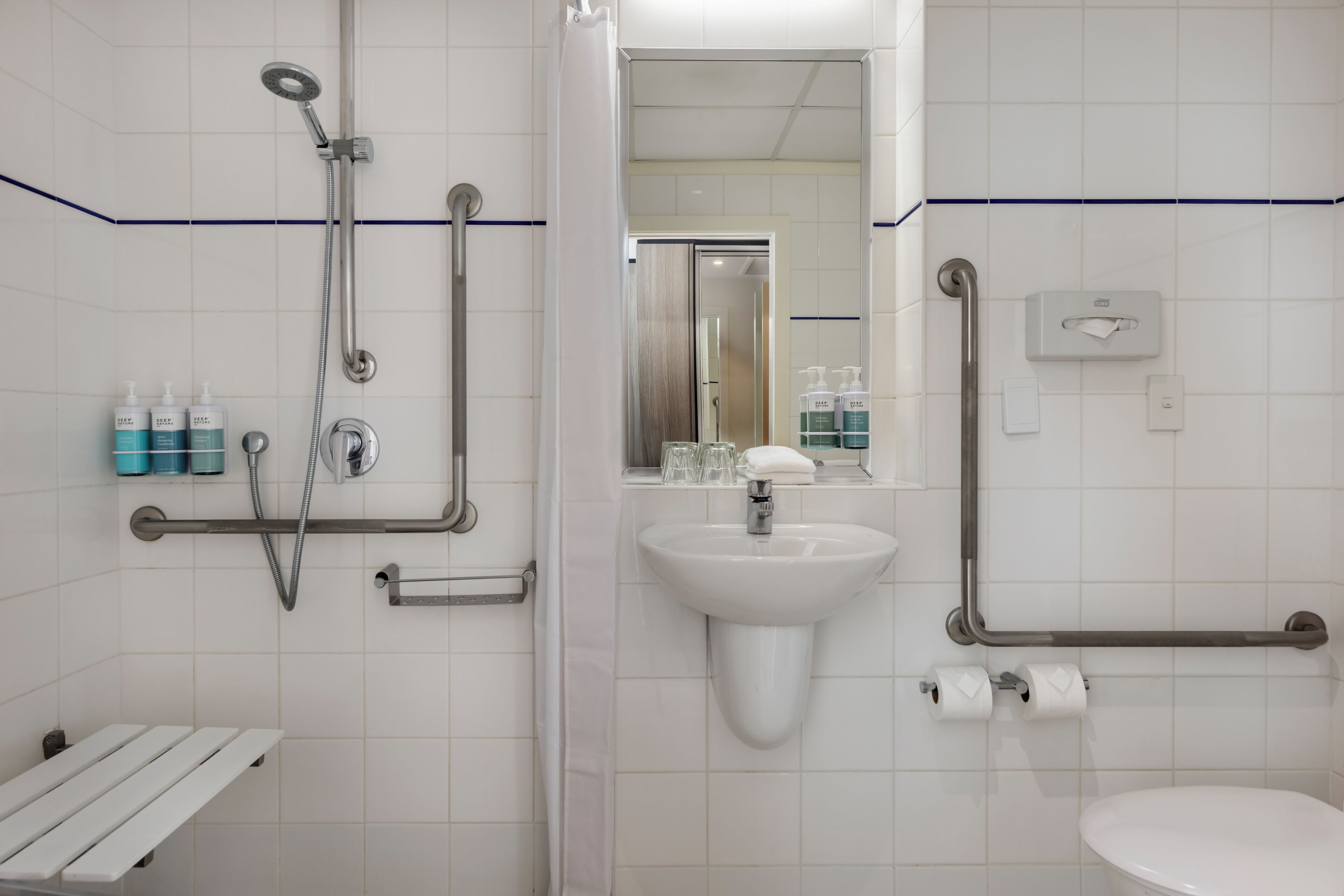 A bathroom with a sink, toilet, shower, and grab bars.