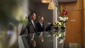 A reception area with a glass counter, two people standing behind it, and a wooden door in the background. - Novotel Wellington (Wellington)