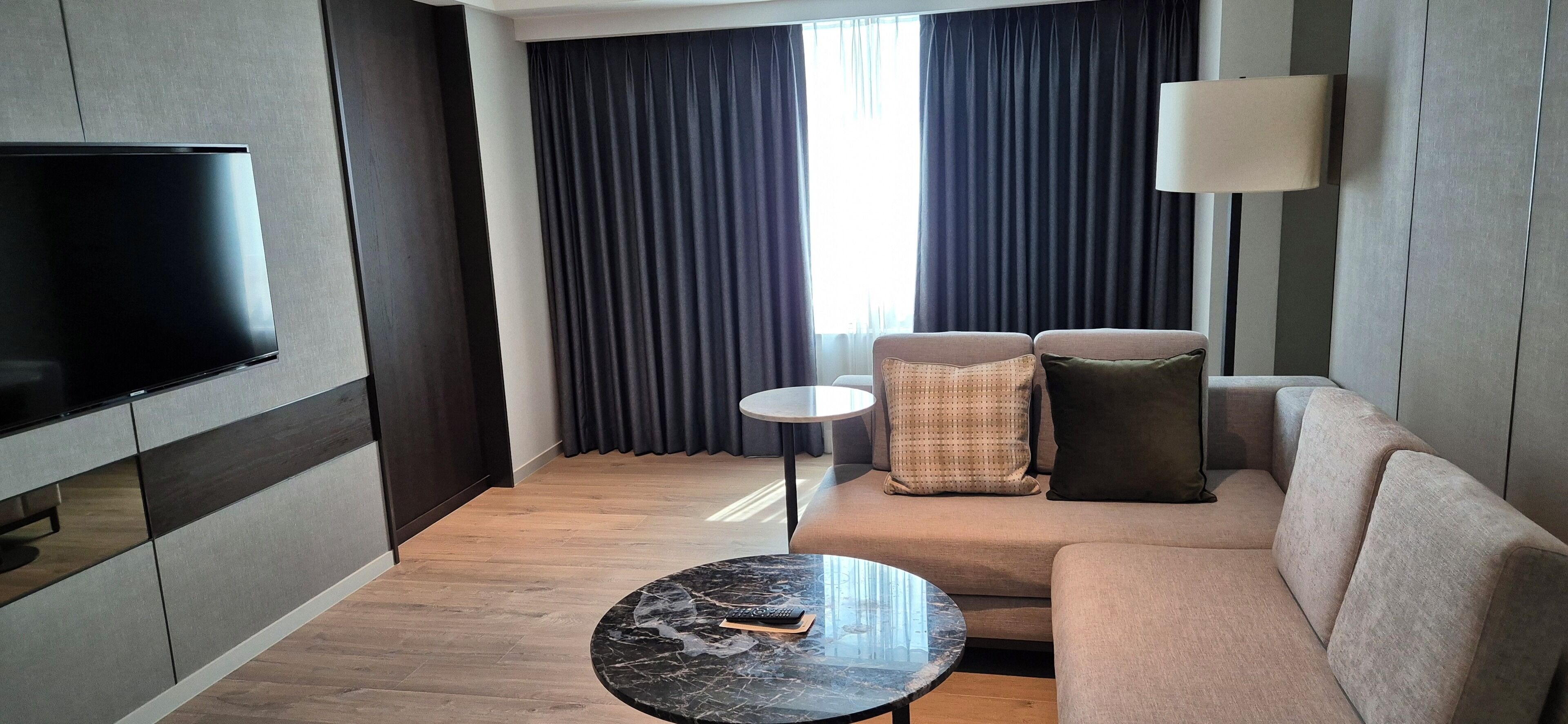 Et moderne hotelværelse med et fladskærms-tv, en sofa, et rundt sofabord og en lampe.