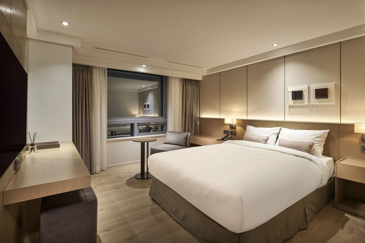 A modern hotel room with a large bed, a desk, and a window with curtains.
