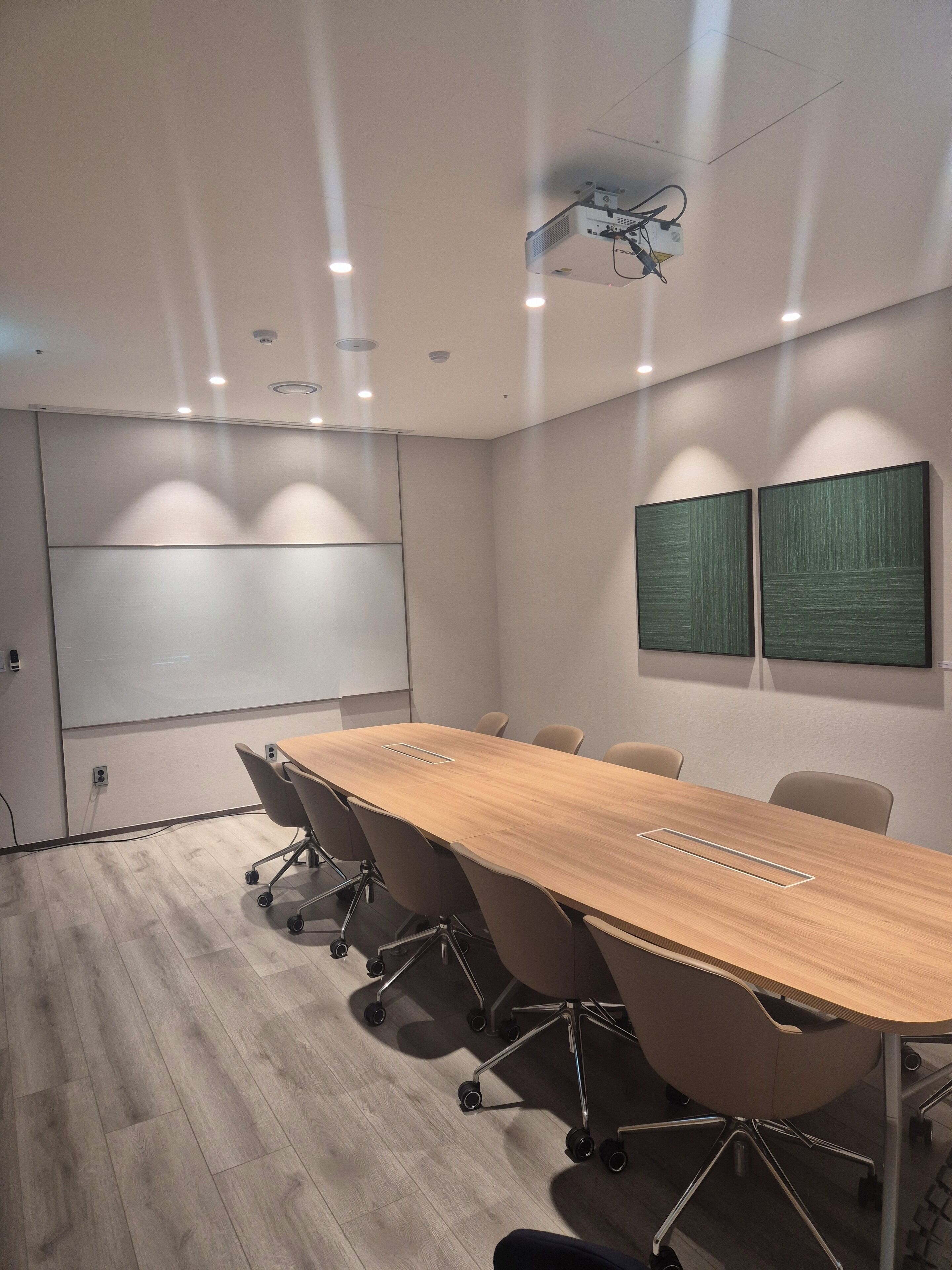 Uma sala de conferências com uma mesa comprida, seis cadeiras, um projetor e duas pinturas abstratas na parede.