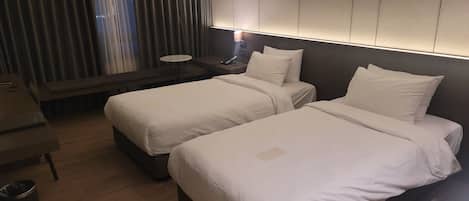 A hotel room with two beds, a desk, and a nightstand with a lamp.