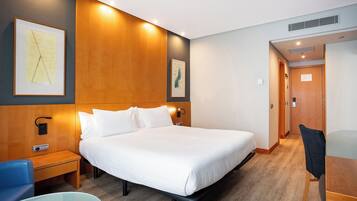 A hotel room with a large bed, a bedside table, a chair, and artwork on the walls.