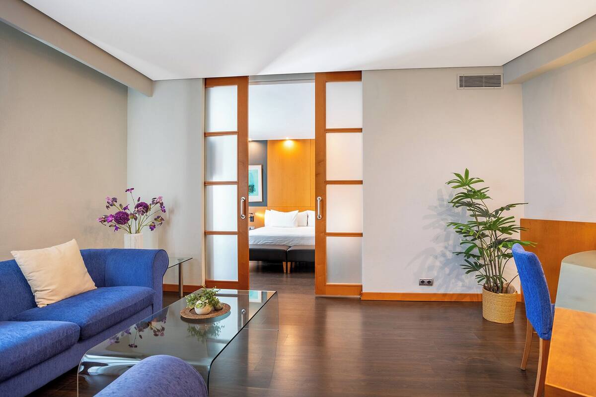 Een moderne hotelkamer met een bank, een glazen salontafel, een bed en een potplant.