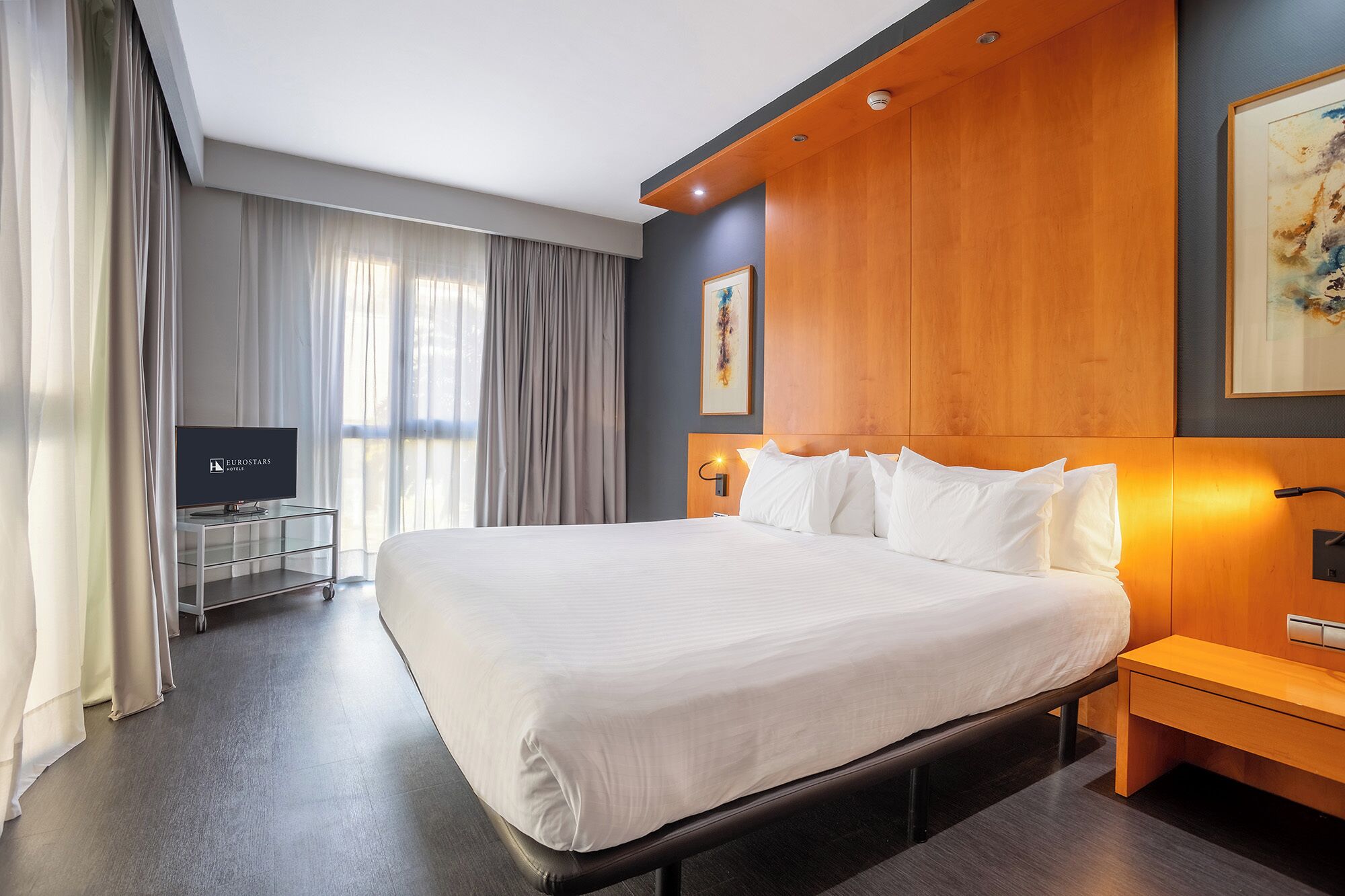 A modern hotel room with a large bed, a television, and a wooden headboard.