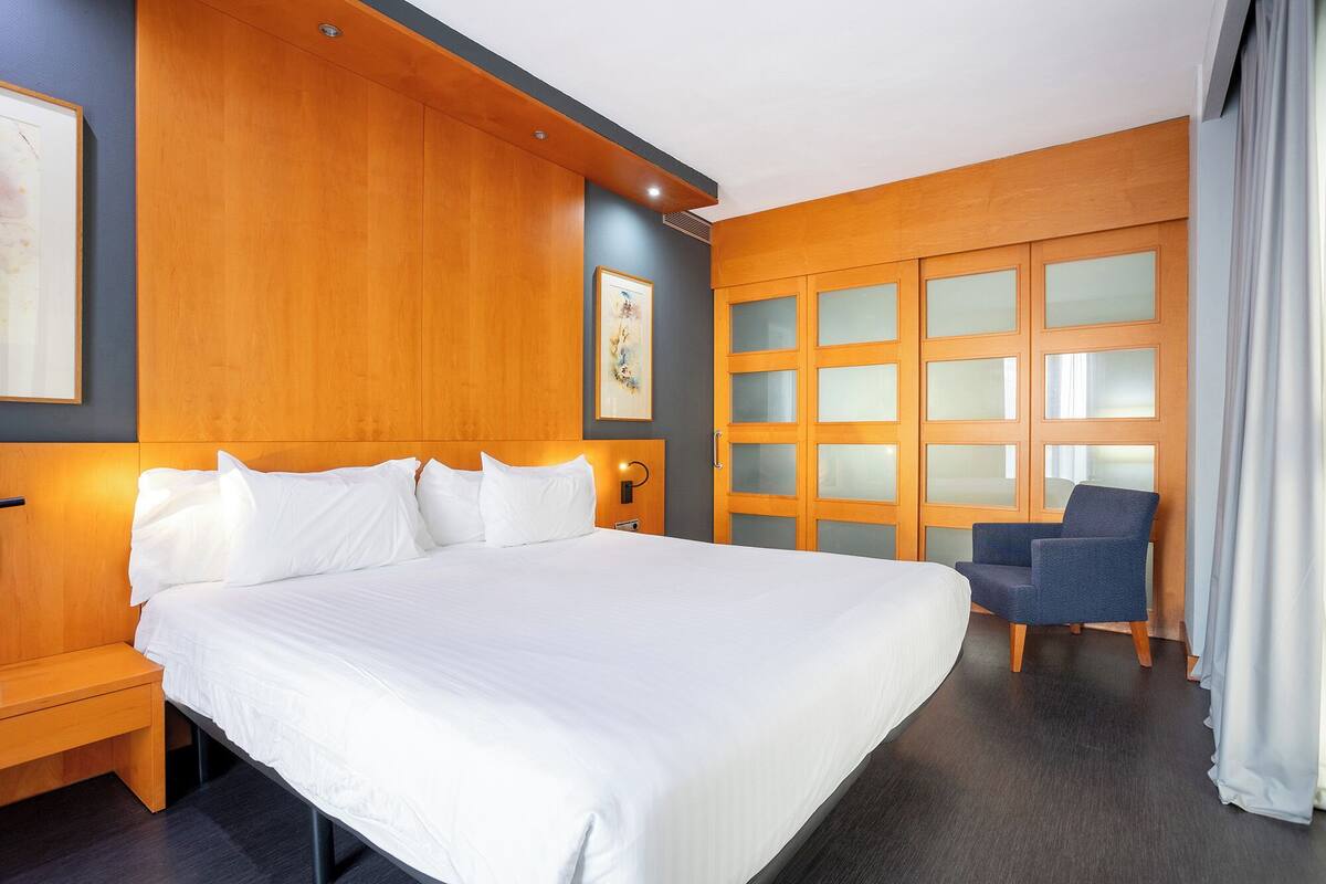 Een hotelkamer met een groot bed, een zithoek met een stoel en een muur met een ingelijste foto.