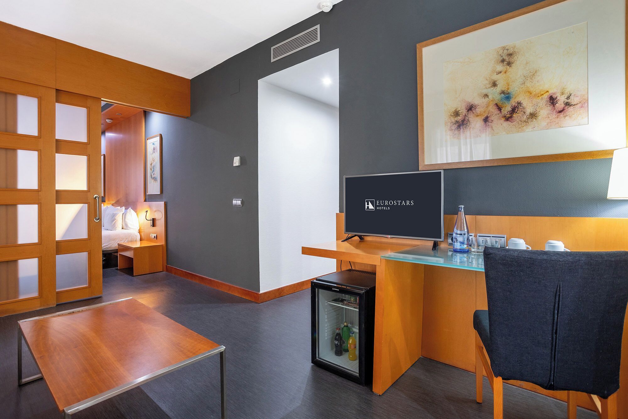 Ett modernt hotellrum med ett skrivbord i trä, en tv, ett minikylskåp och en säng med utsikt.
