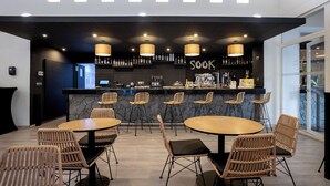 A modern bar area with a black counter, multiple seating options including round tables and wicker chairs, and a visible bar stocked with various bottles. - Eurostars Atlantida (Santa Cruz de Tenerife)