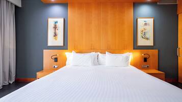 A hotel room with a large bed, wooden headboard, two bedside tables with lamps, and two framed artworks on the walls.
