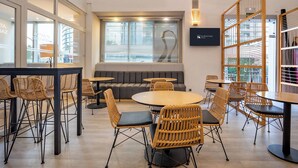 A modern hotel lobby with round tables, wicker chairs, a sofa, and a television screen displaying the hotel name. - Eurostars Atlantida (Santa Cruz de Tenerife)