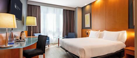 Een hotelkamer met een bed, een bureau, een stoel, een lamp en een groot raam met gordijnen.