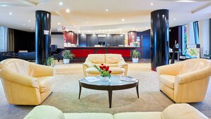 A hotel lobby with leather sofas, a reception desk, and a large potted plant. - Hotel Clorinda (Capaccio-Paestum)