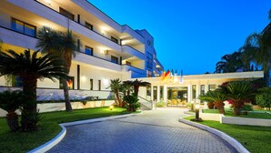 A modern hotel with a paved entrance, palm trees, and a well-lit facade. - Hotel Clorinda (Capaccio-Paestum)