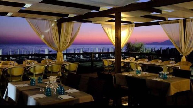 An outdoor dining area with tables and chairs, draped with sheer curtains, overlooking a cityscape at sunset. - Hotel Clorinda (Capaccio-Paestum)