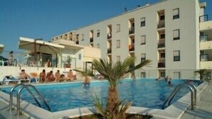 A swimming pool with a palm tree in the center, surrounded by a building with multiple balconies. - Hotel Duca degli Abruzzi (Montesilvano)