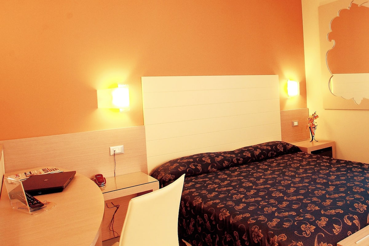 A hotel room with a bed, bedside tables, a desk with a laptop, and a chair.