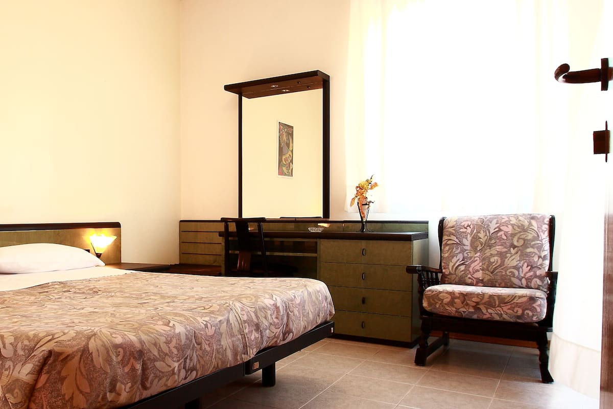 A hotel room with a bed, a chair, a dresser, a mirror, and a painting on the wall.