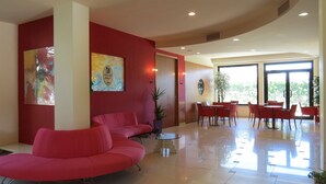 A modern hotel lobby with a red sofa, a glass coffee table, and a dining area with red chairs. - Hotel Duca degli Abruzzi (Montesilvano)