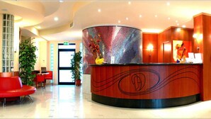 A reception area with a curved wooden desk, a large potted plant, and red chairs. - Hotel Duca degli Abruzzi (Montesilvano)