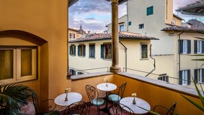 Un balcón con mesa y sillas, con vistas a un paisaje urbano con edificios y cielo despejado.