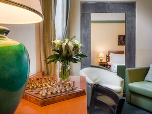 A hotel room with a chessboard, a vase with flowers, a lamp, and a bed with a green headboard.