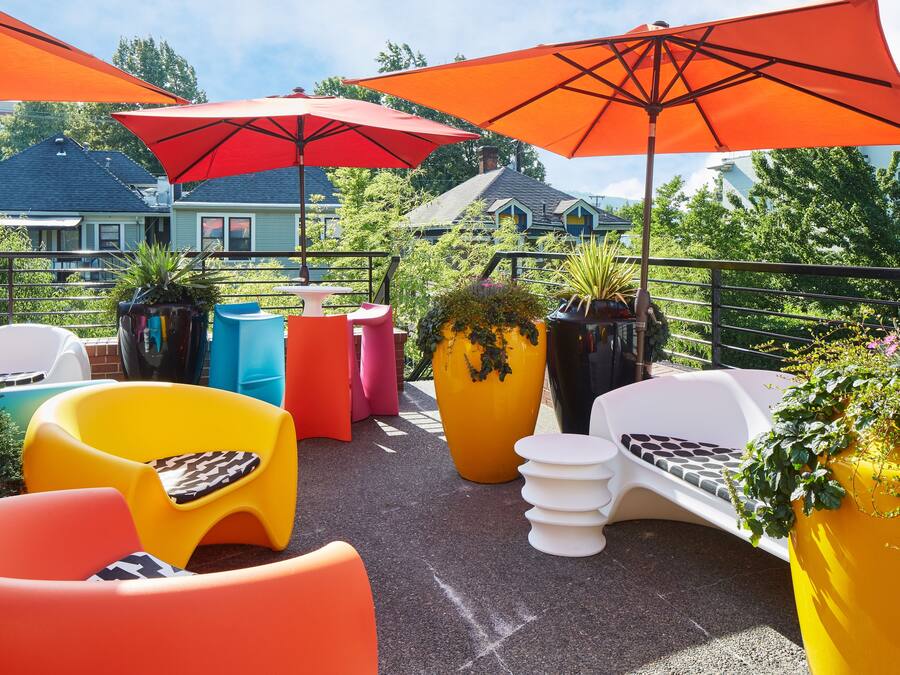 A rooftop patio with colorful chairs, large potted plants, and red umbrellas.