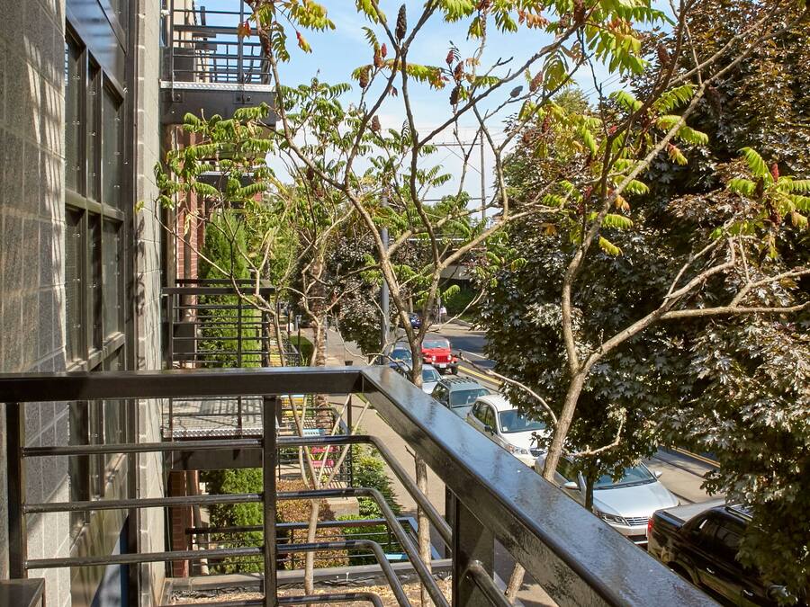 Un balcó amb baranes metàl·liques que donen a un carrer amb cotxes aparcats i arbres.