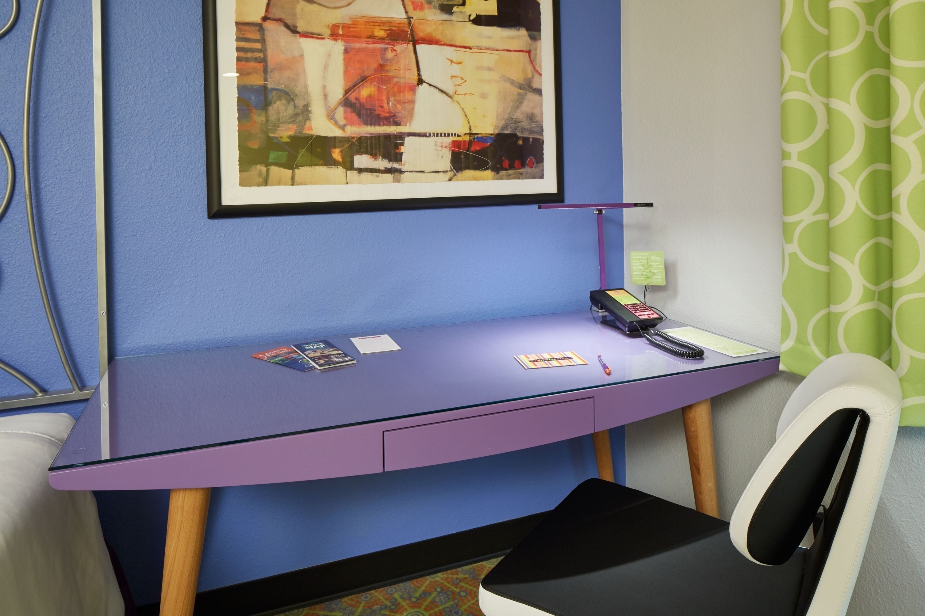 A room with a purple desk, a framed abstract painting, a telephone, and a chair.
