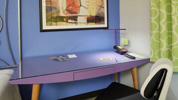 A room with a purple desk, a framed abstract painting, a telephone, and a chair.