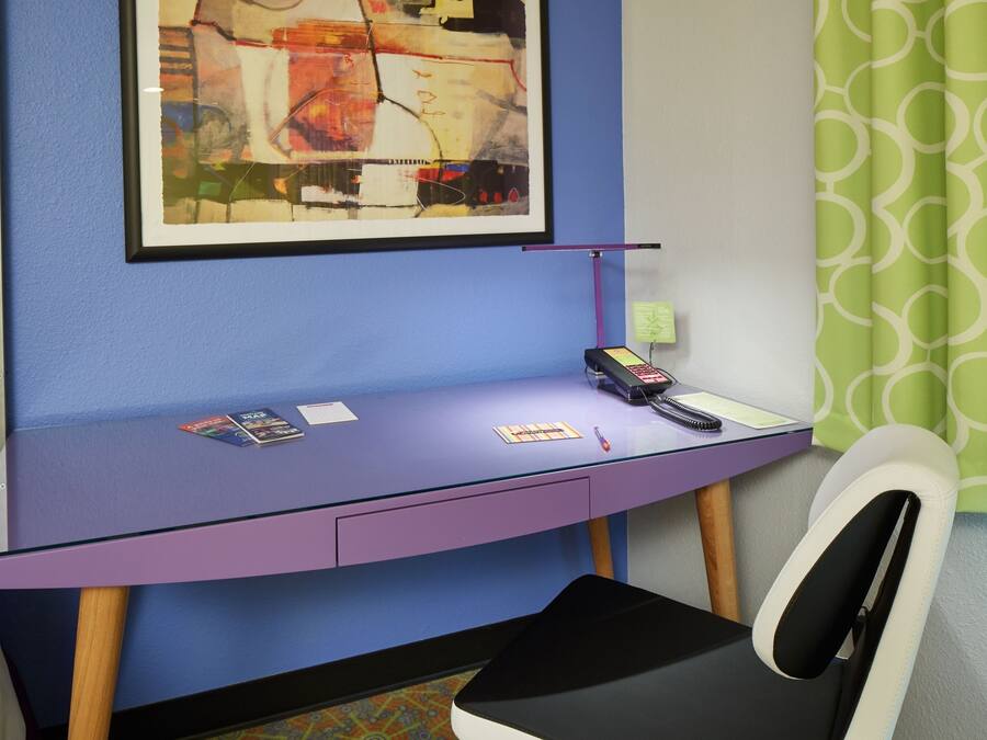 A room with a purple desk, a framed abstract painting, a telephone, and a chair.