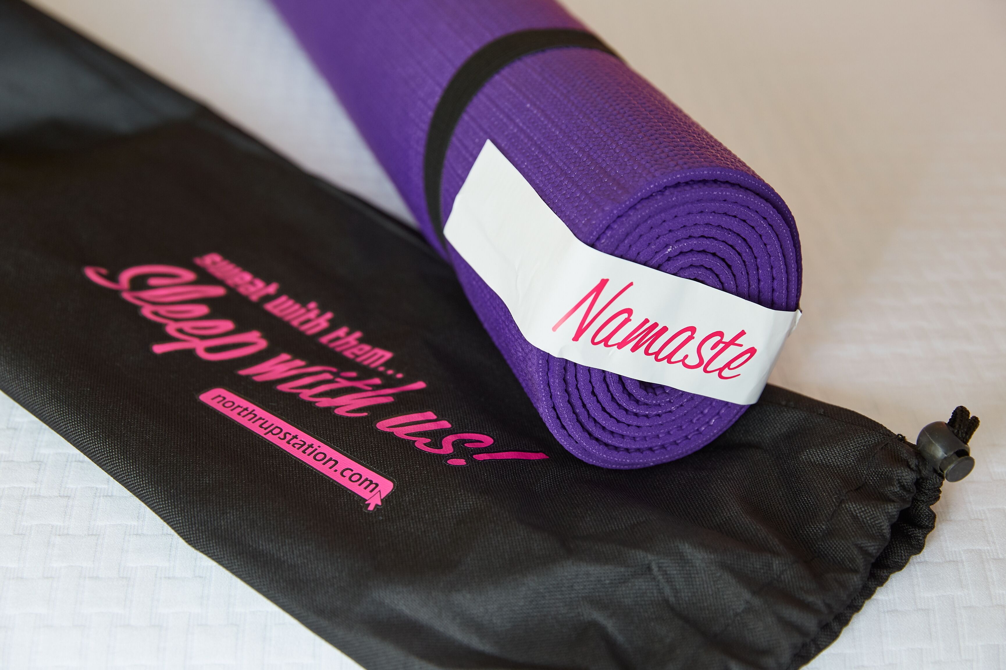 Una colchoneta morada enrollada con la etiqueta "Namaste" y una colchoneta negra con texto rosa.