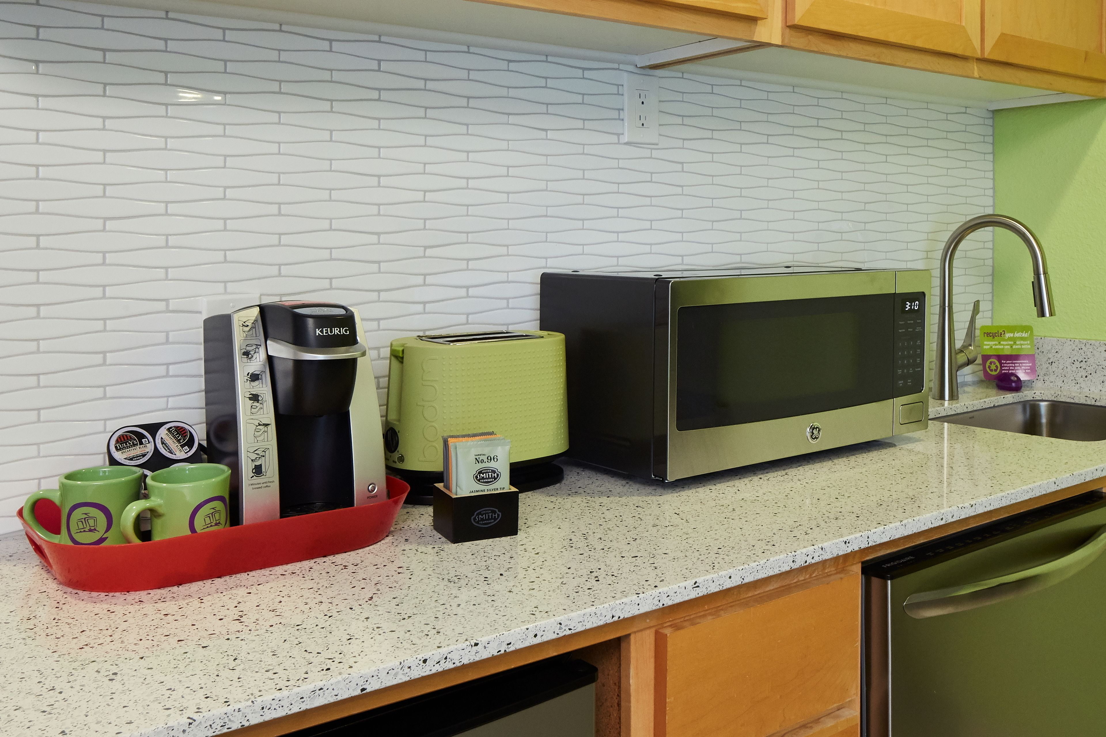 Une cuisine équipée d’un four à micro-ondes, d’un grille-pain, d’une machine à café et d’un plateau rouge avec des tasses vertes.