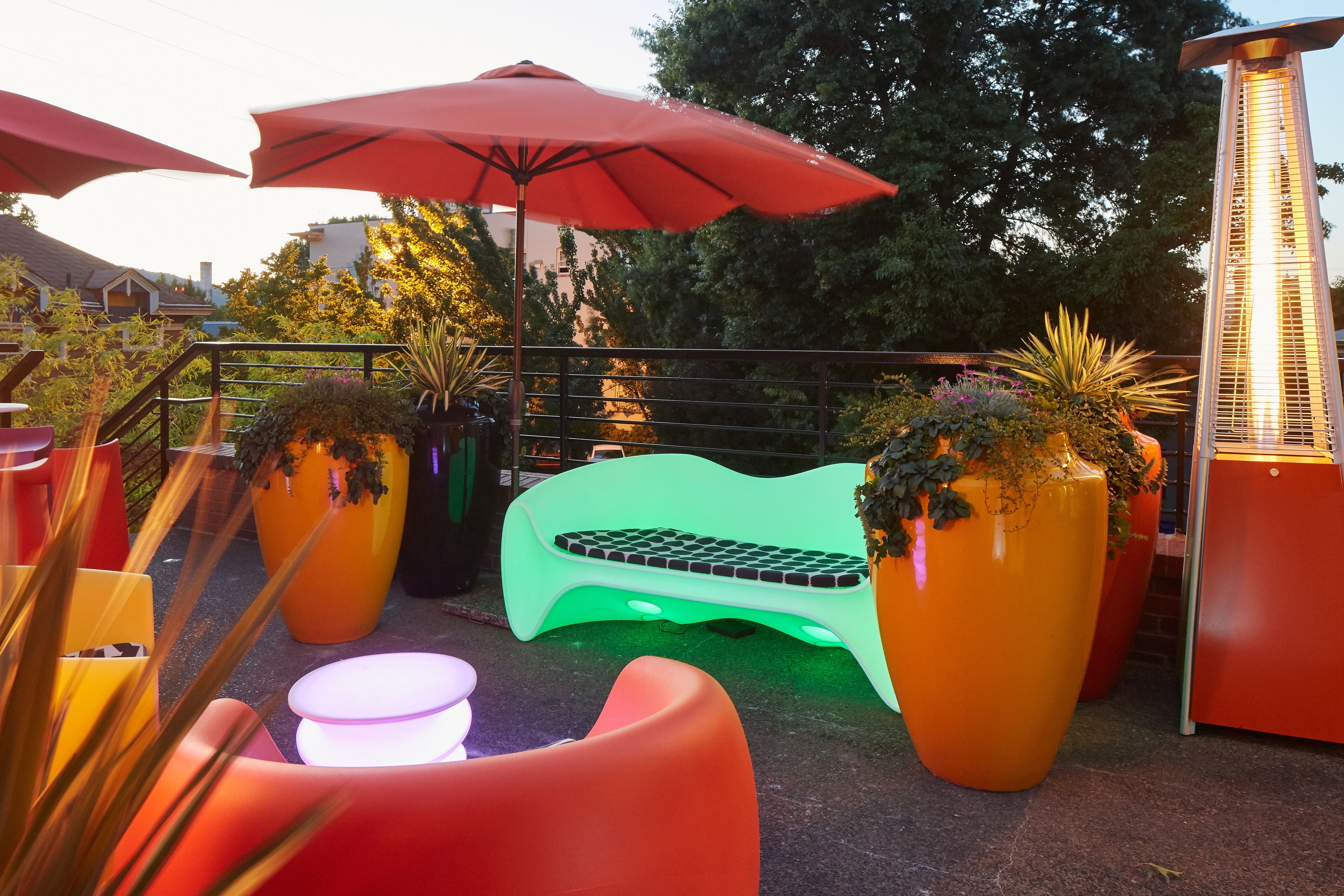 A patio area with a green bench, red umbrellas, and potted plants.