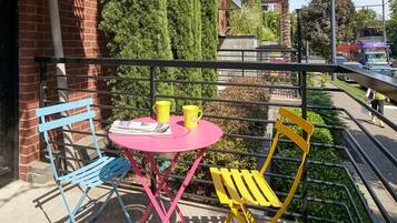 A balcony with a pink table and two chairs, one blue and one yellow.