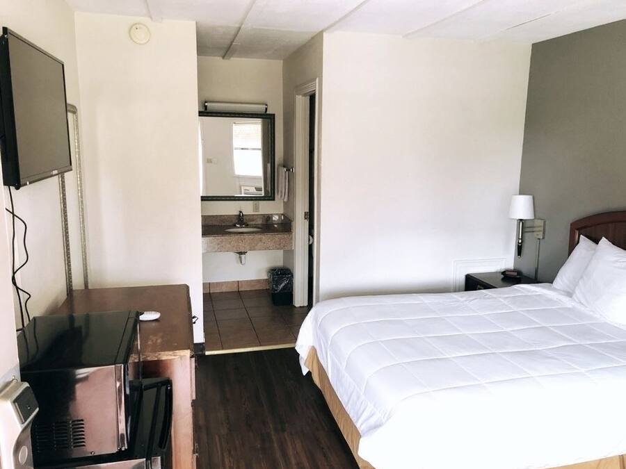 Hotellihuone, jossa on sänky, työpöytä, televisio, kylpyhuone ja yöpöytä.