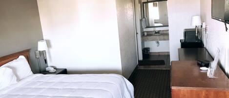 Hotelkamer met een groot bed, een bureau, een spiegel en een badkamer die door een geopende deur zichtbaar is.