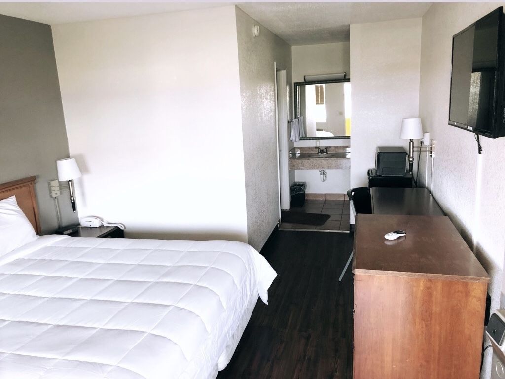 A hotel room with a bed, a desk, a mirror, and a television.