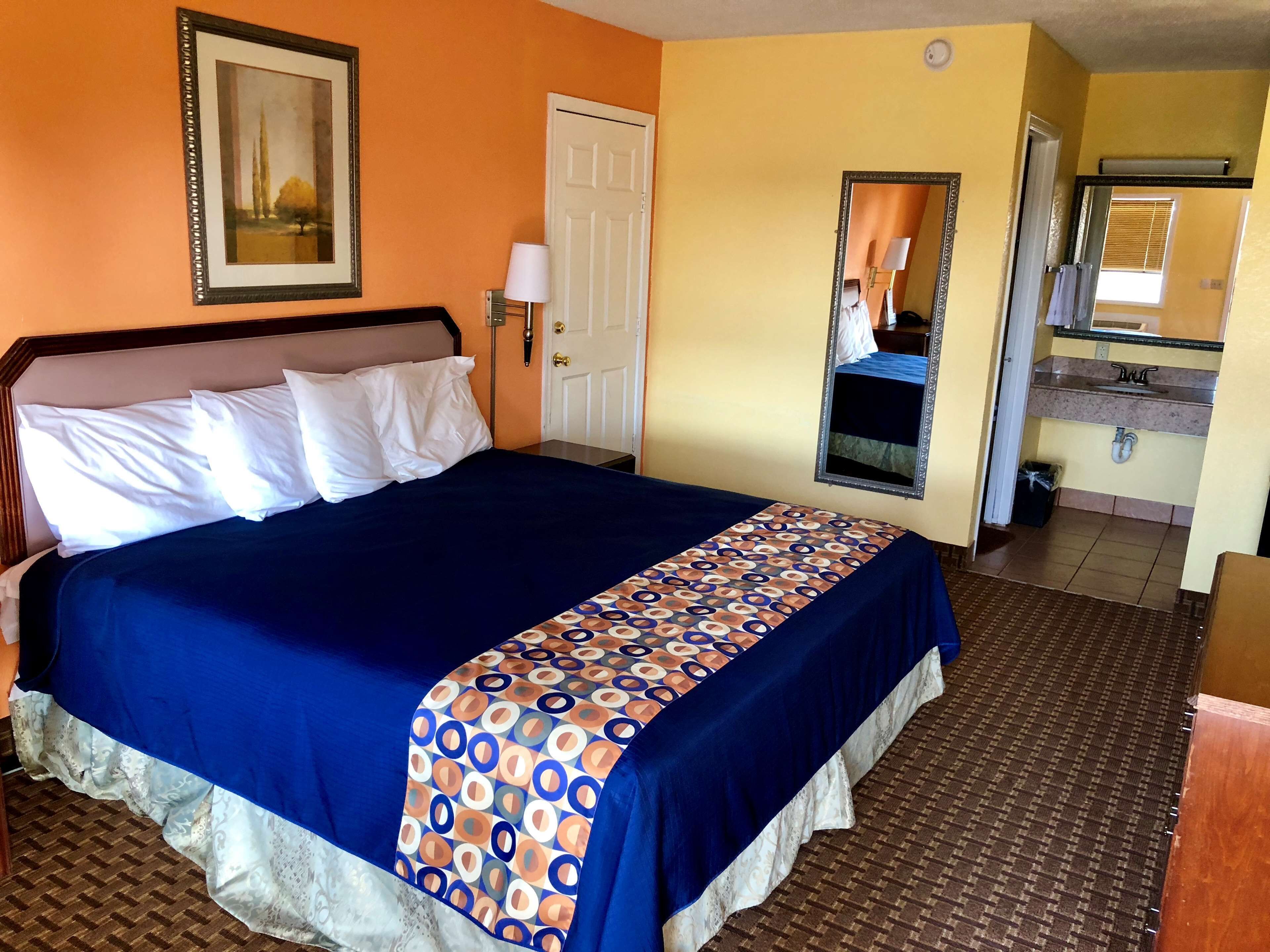 Hotelkamer met een groot bed, een deur, een spiegel en een zichtbare badkamer door een geopende deur.