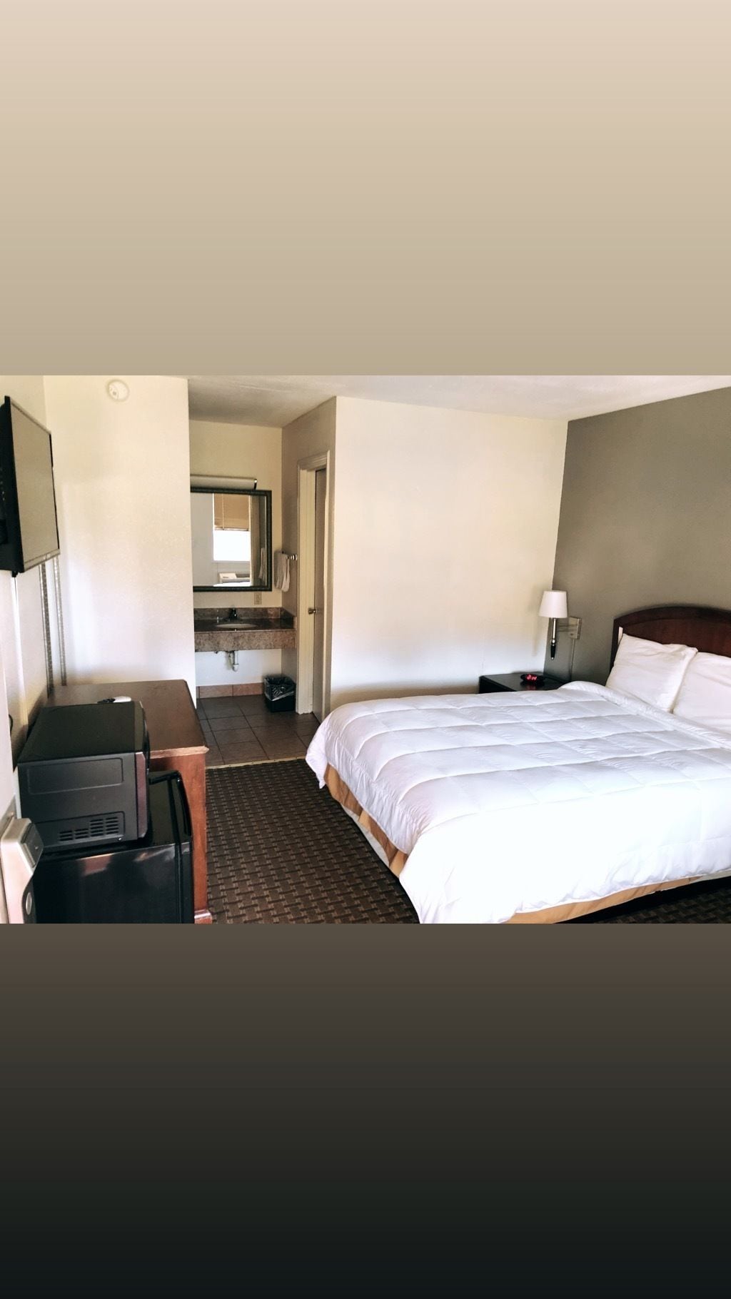 Habitación de hotel con cama, escritorio, silla, televisor y baño visible a través de una puerta abierta.