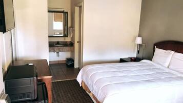 Habitación de hotel con cama, escritorio, silla, televisor y baño visible a través de una puerta abierta.
