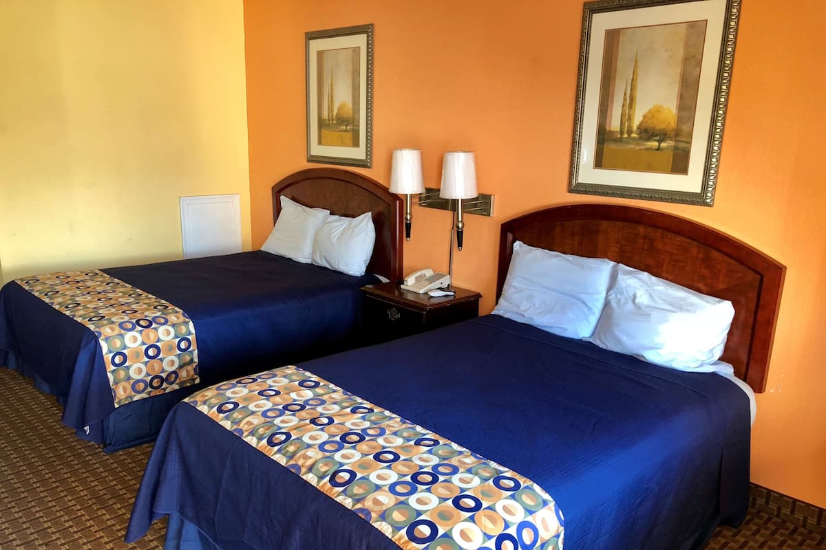 Dos camas matrimoniales con ropa de cama azul a juego y almohadas decorativas estampadas, una mesita de noche con lámpara y obras de arte enmarcadas en las paredes.
