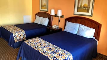 Dos camas matrimoniales con ropa de cama azul a juego y almohadas decorativas estampadas, una mesita de noche con lámpara y obras de arte enmarcadas en las paredes.