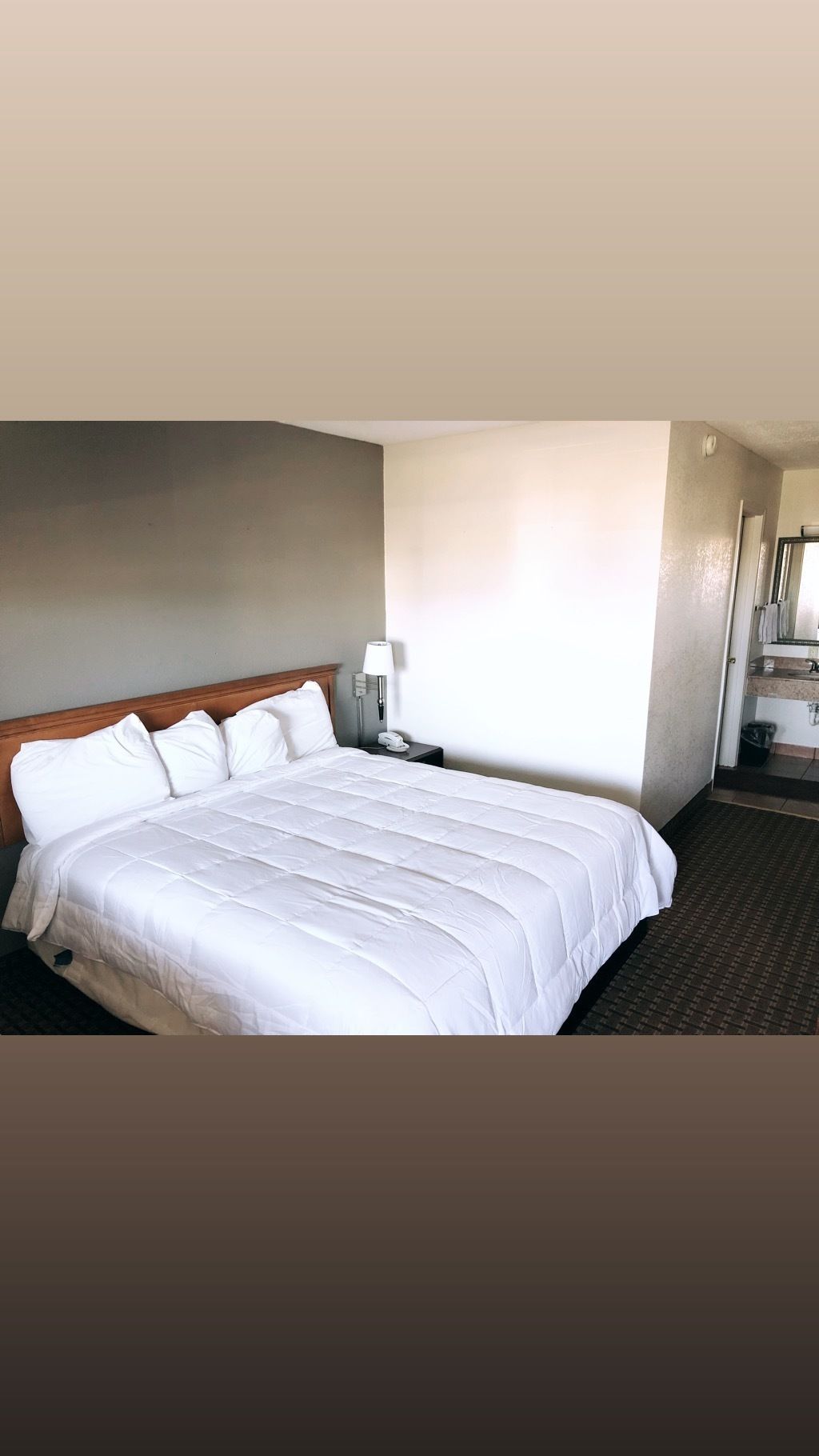 Camera d'albergo con un letto grande, un comodino, una lampada e un bagno visibile attraverso una porta aperta.