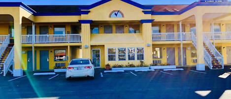 Un motel à deux étages, avec une façade jaune, une entrée centrale et un parking.