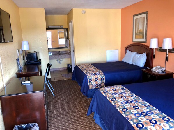 A hotel room with two beds, a desk with a chair, a telephone, and a picture on the wall.