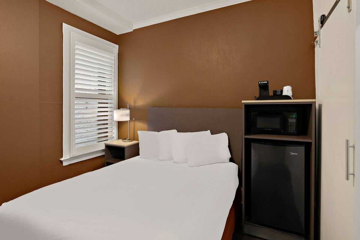 A hotel room with a bed, a nightstand, a microwave, and a refrigerator.